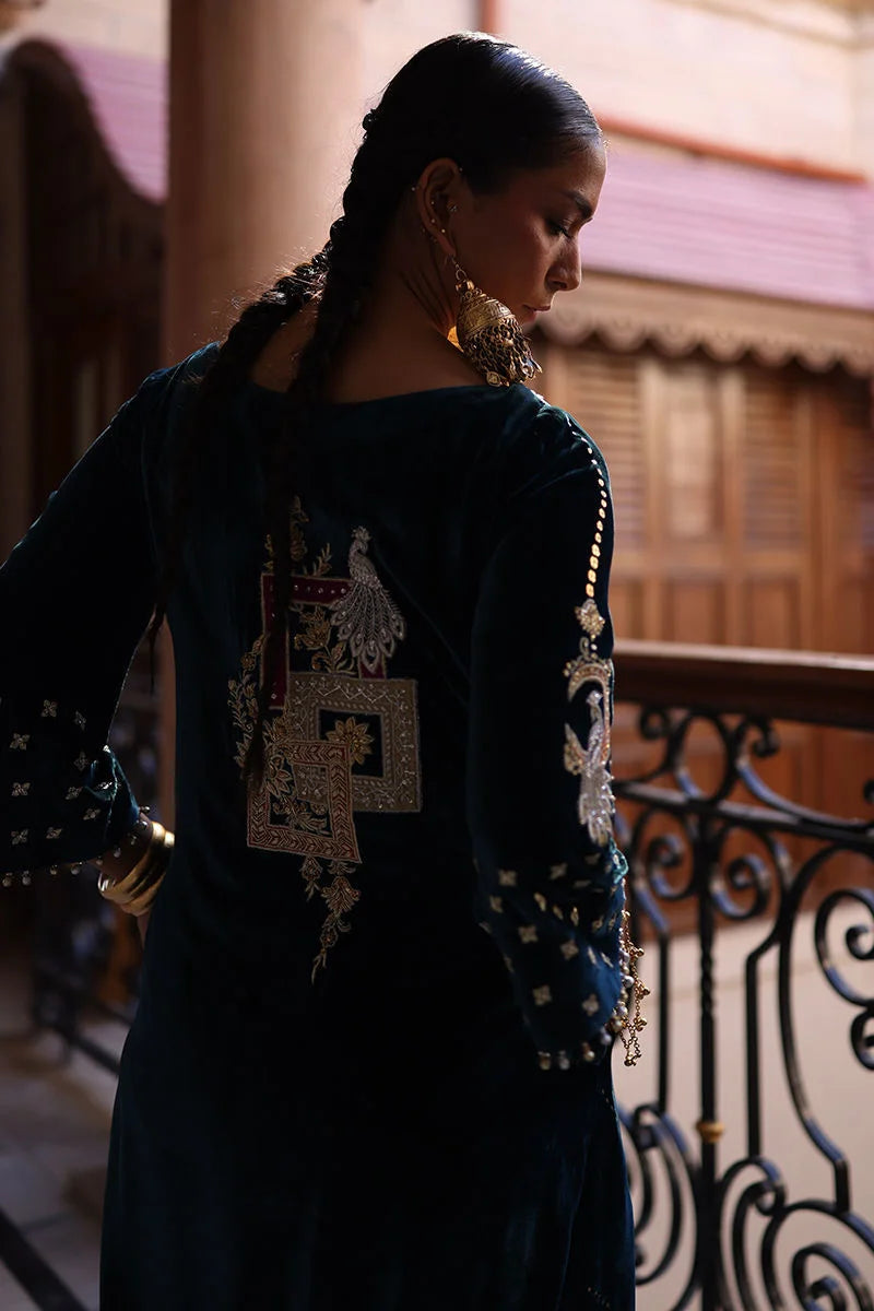 Woman in a dark blue traditional outfit with decorative elements, standing on a balcony.