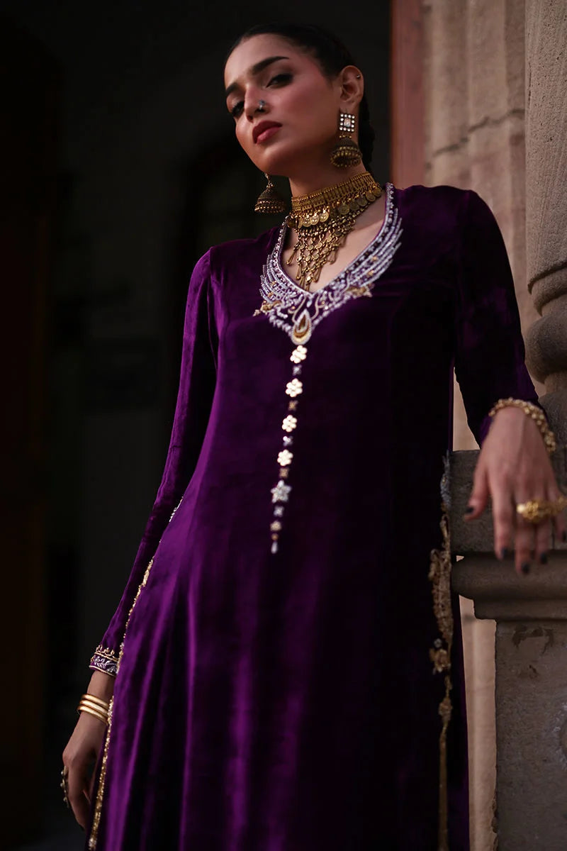 Woman in a purple traditional outfit with gold jewelry against a dark background