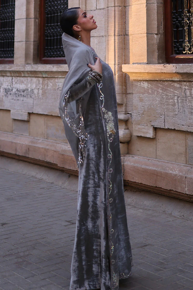 Woman in a long, elegant dress with intricate designs standing in front of a stone building.