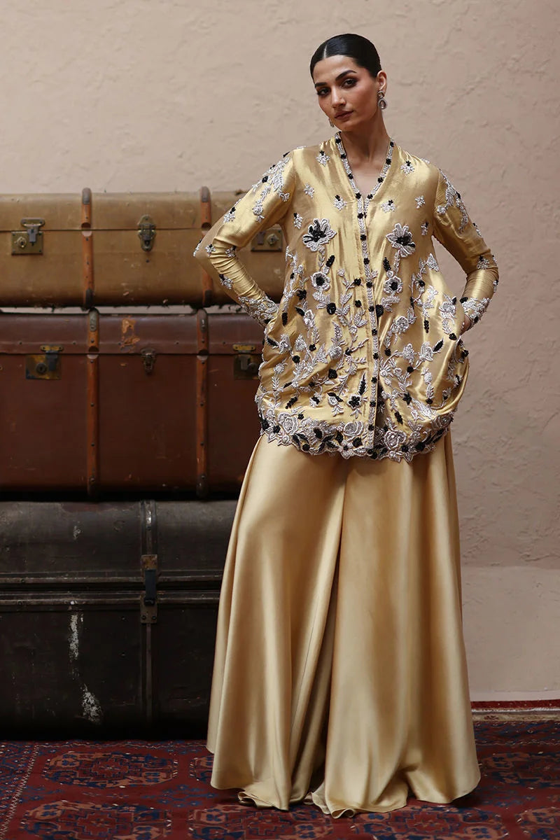 Woman in a gold embroidered outfit standing next to vintage suitcases.