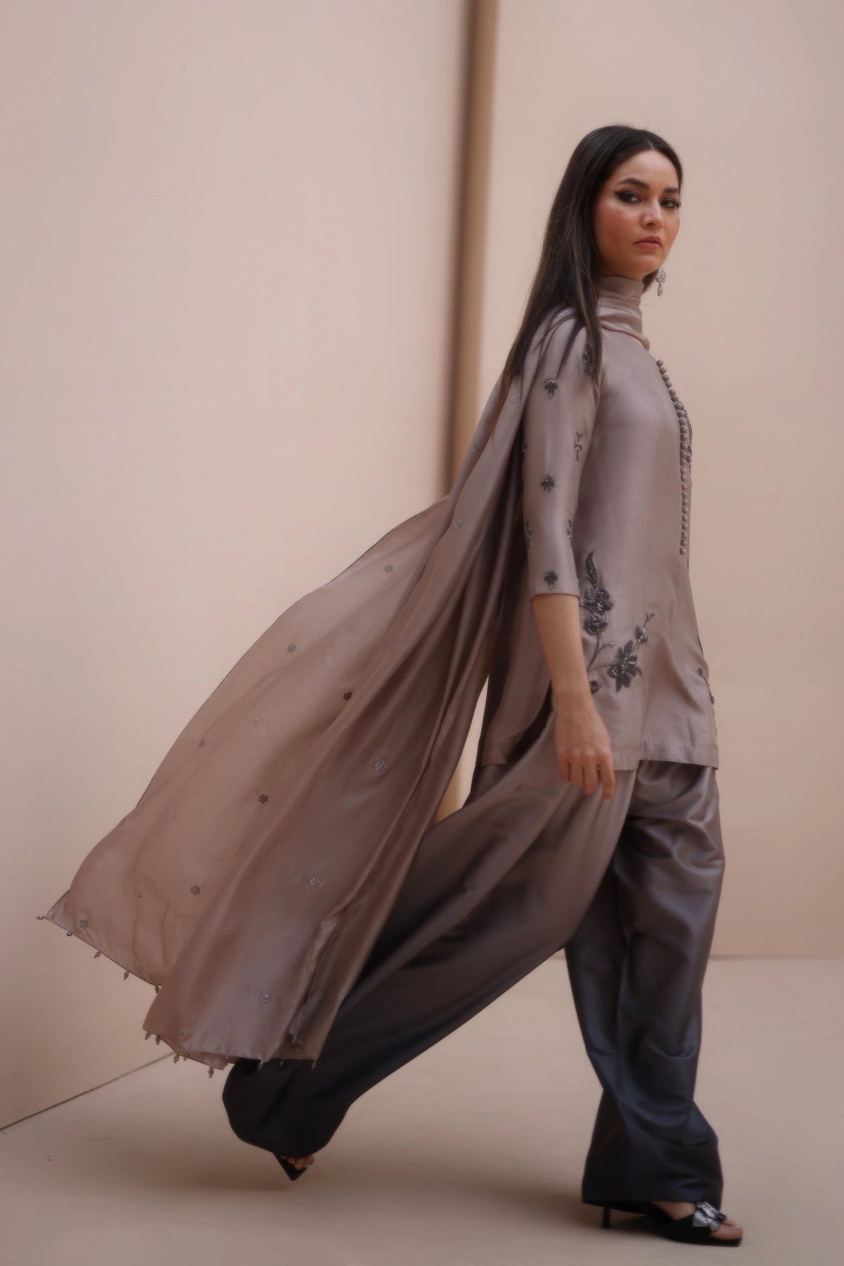 Woman wearing a long beige scarf and gray outfit against a beige background
