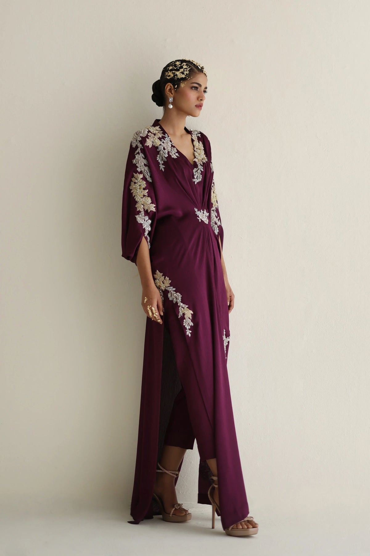 Woman wearing a purple dress with floral embellishments against a plain background