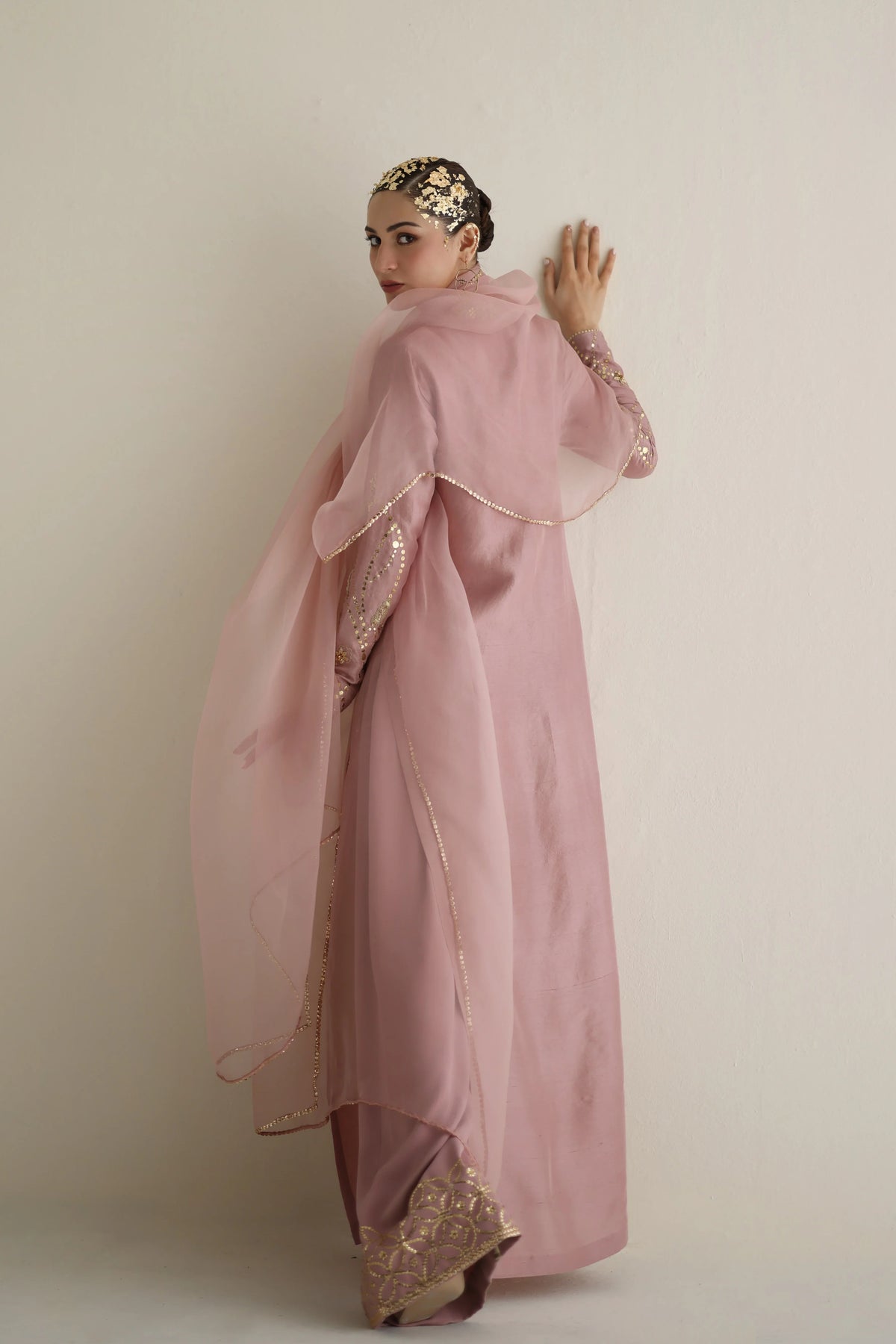 Woman wearing a pink traditional outfit with gold embroidery against a plain background