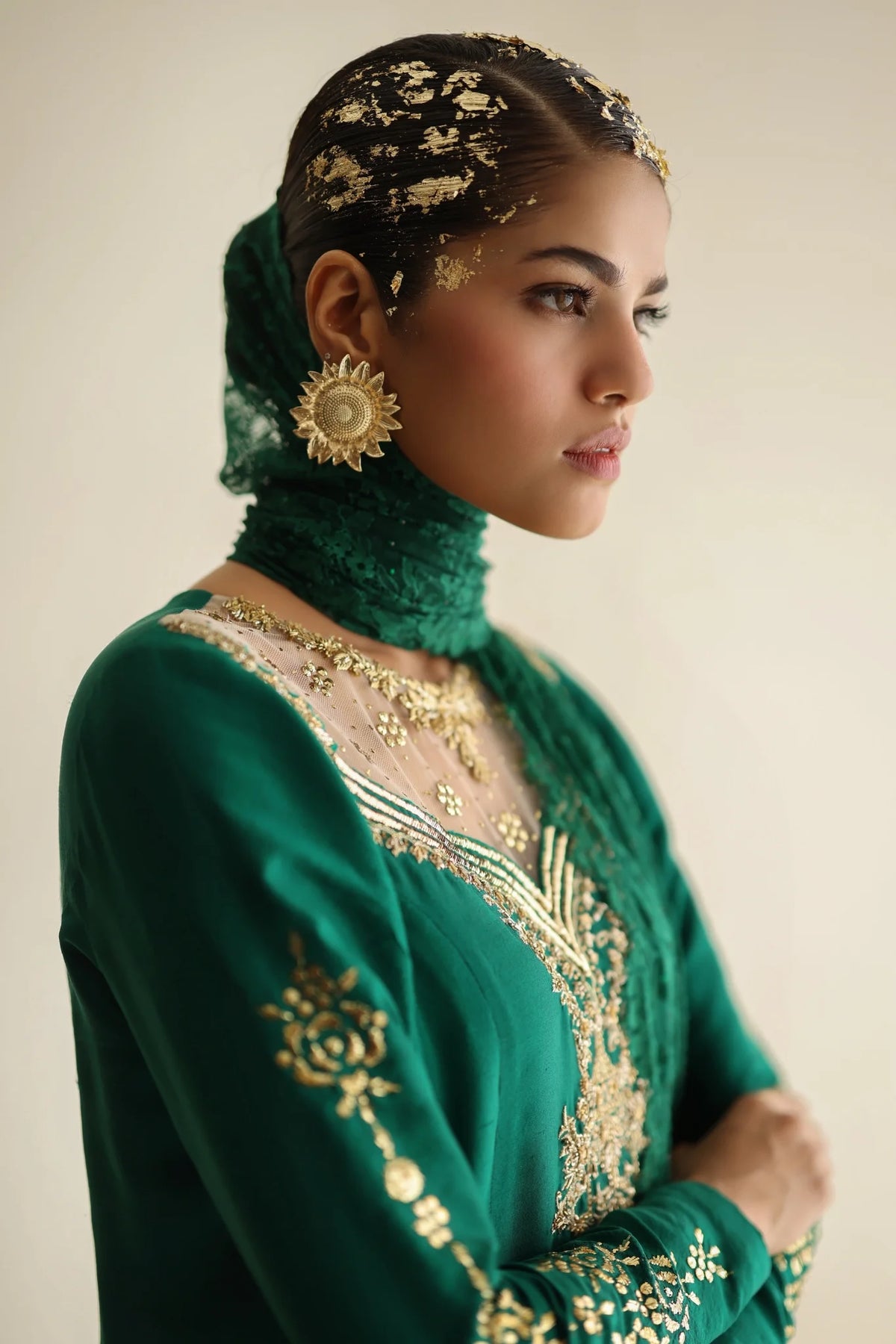 Woman wearing a green embroidered outfit with gold details on a plain background