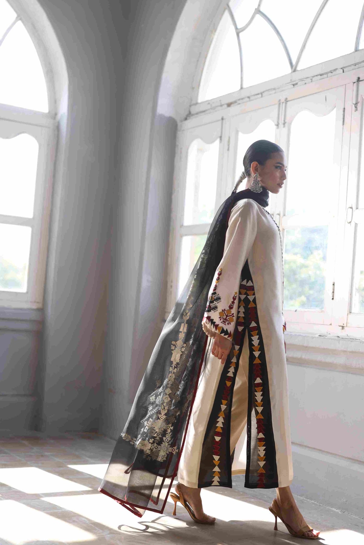 Woman in a stylish outfit with a long, patterned scarf in a bright room with large windows.
