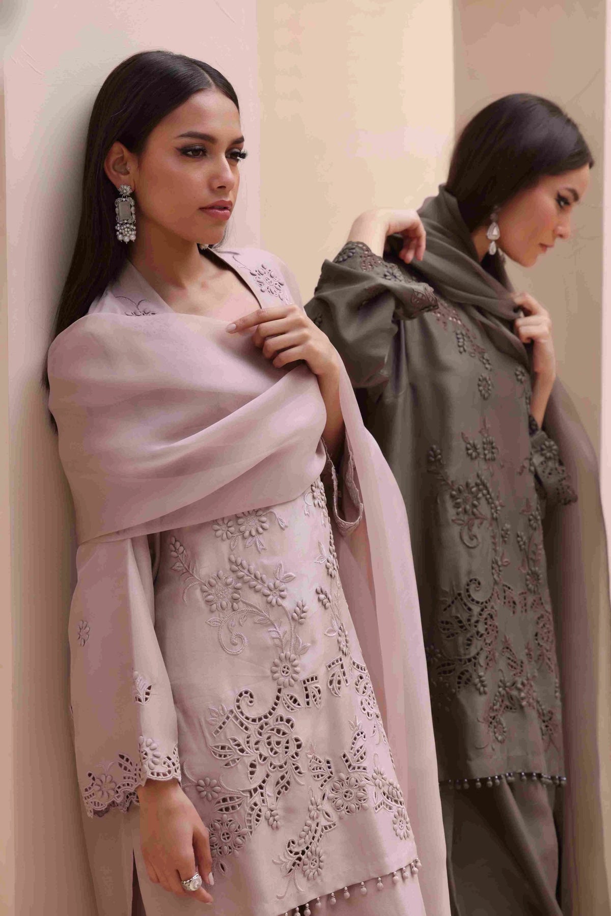 Two women wearing embroidered shawls against a neutral background
