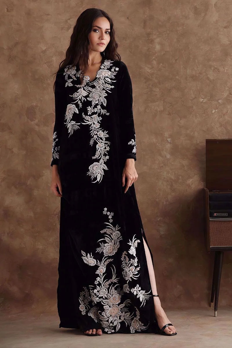 Woman wearing a black dress with white floral embroidery against a brown background