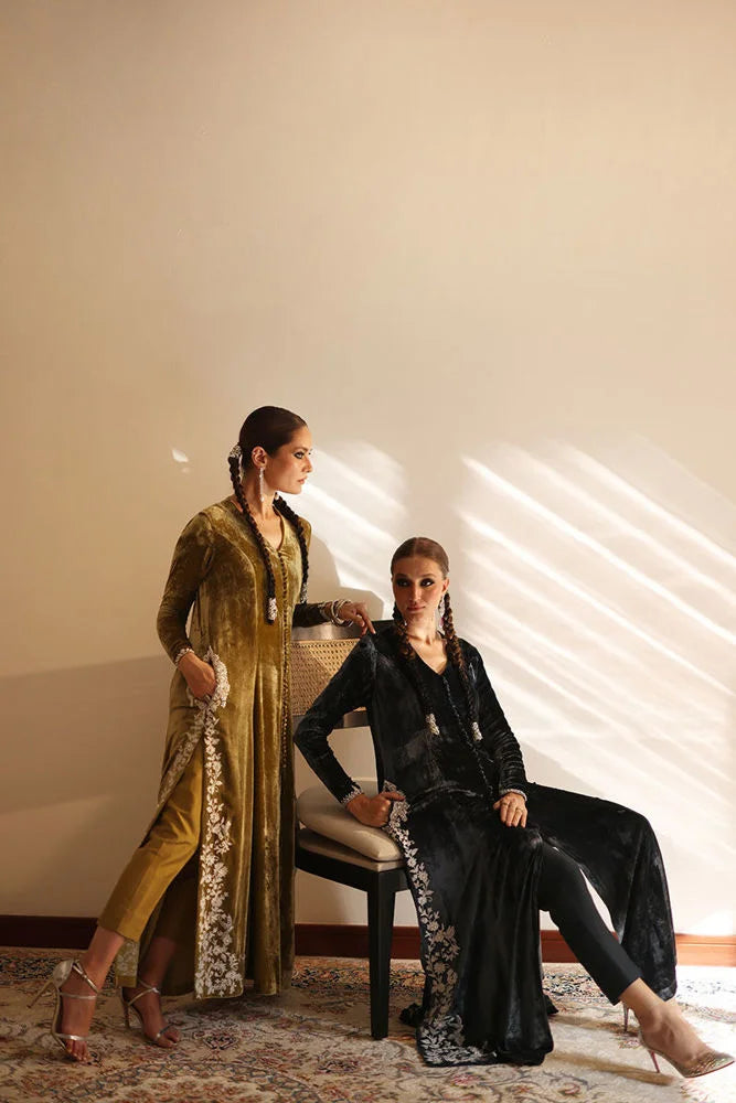 Two women in formal attire sitting on a chair against a neutral wall.