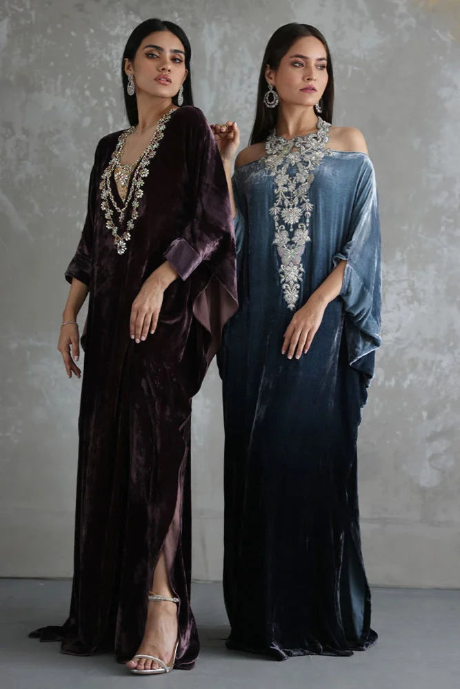 Two women wearing elegant dresses with intricate designs against a plain background