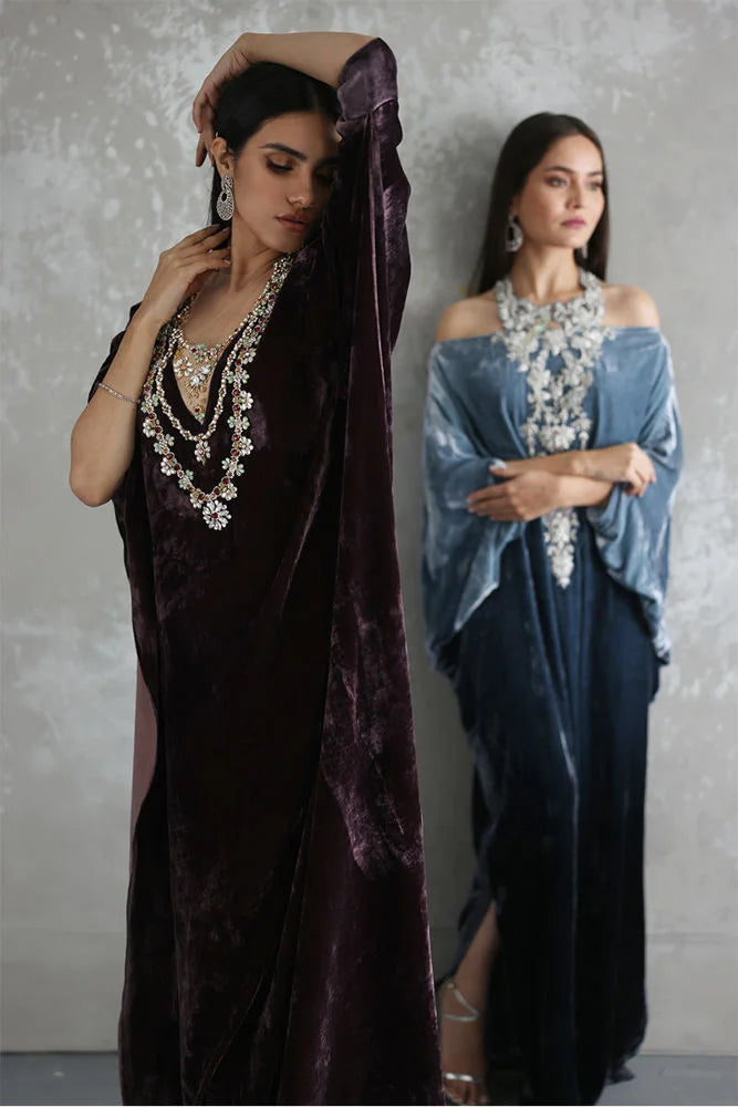Two women wearing elegant dresses with jewelry against a plain background