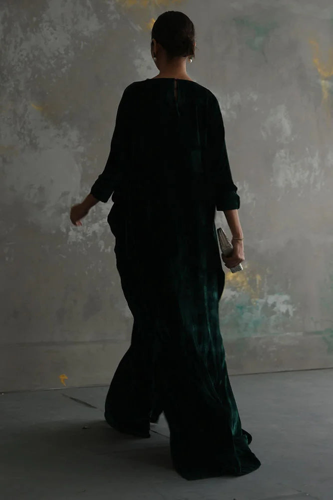 Person wearing a long, dark green dress against a textured wall.