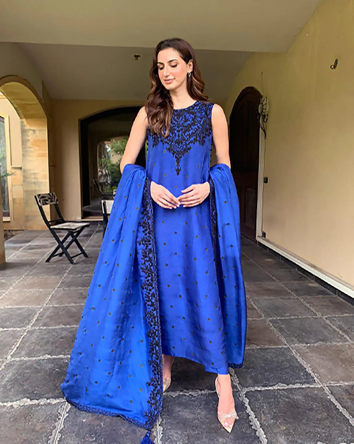 Woman in a blue traditional outfit standing on a stone patio.
