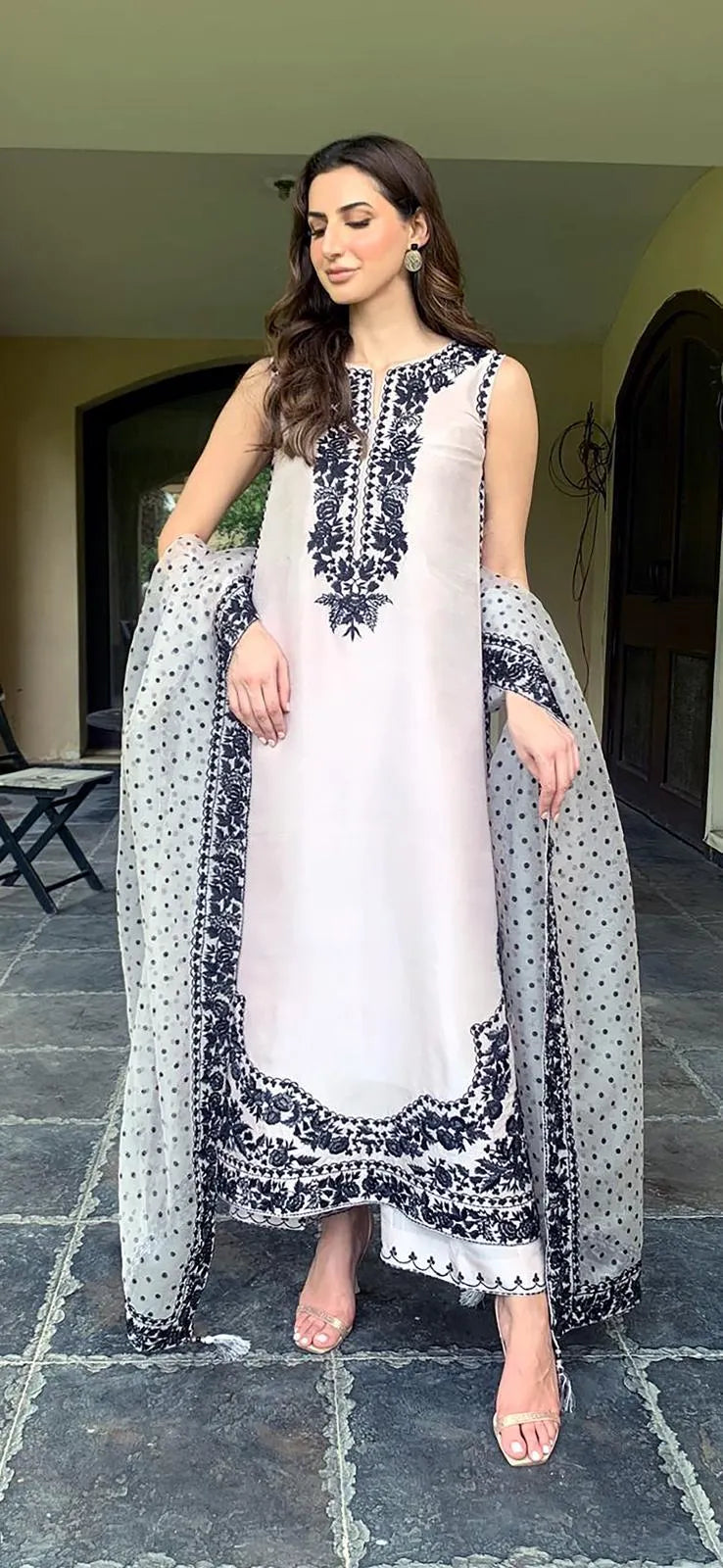 Woman in a traditional outfit with a white and black patterned dress and dupatta standing on a stone path.