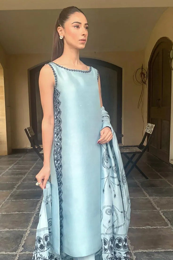 Woman in a light blue traditional outfit with intricate patterns standing in an outdoor setting.