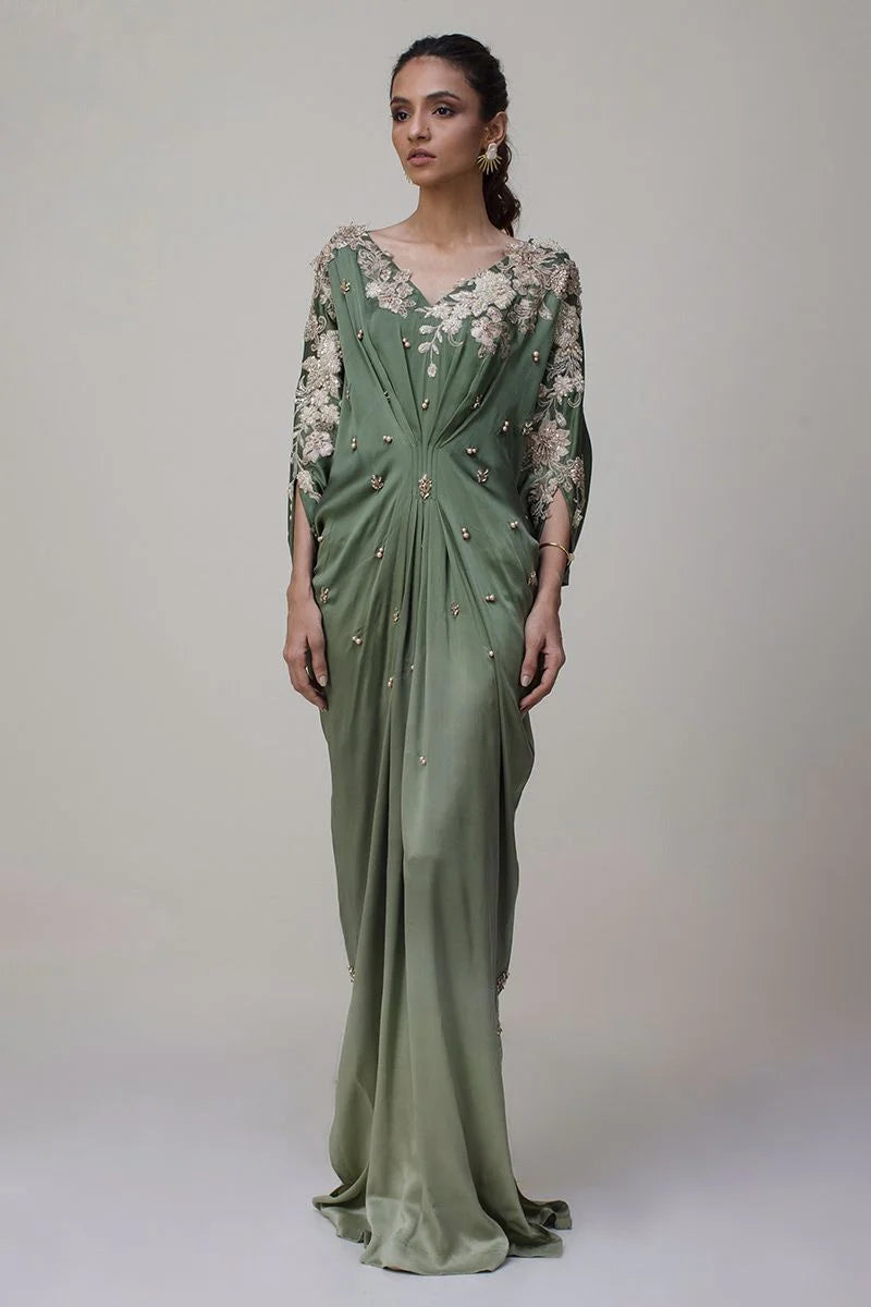 Woman wearing a green evening gown with floral embellishments on a plain background