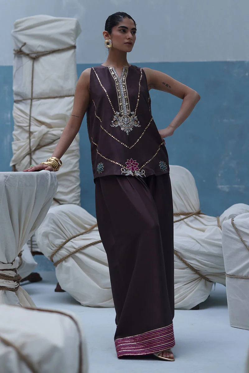 Woman in traditional outfit standing against a blue and white draped fabric background
