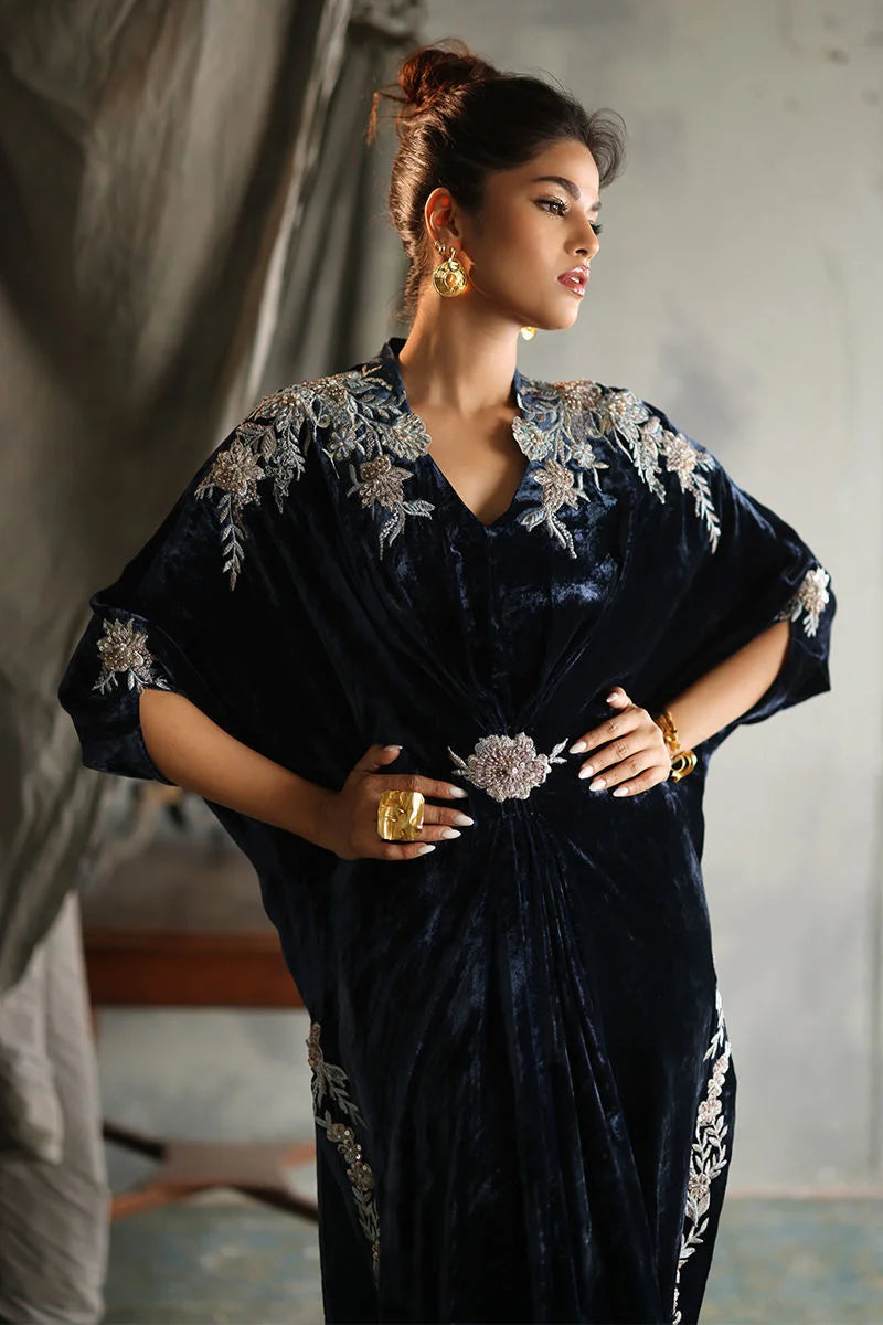 Woman wearing a black embroidered dress with gold jewelry in a neutral setting