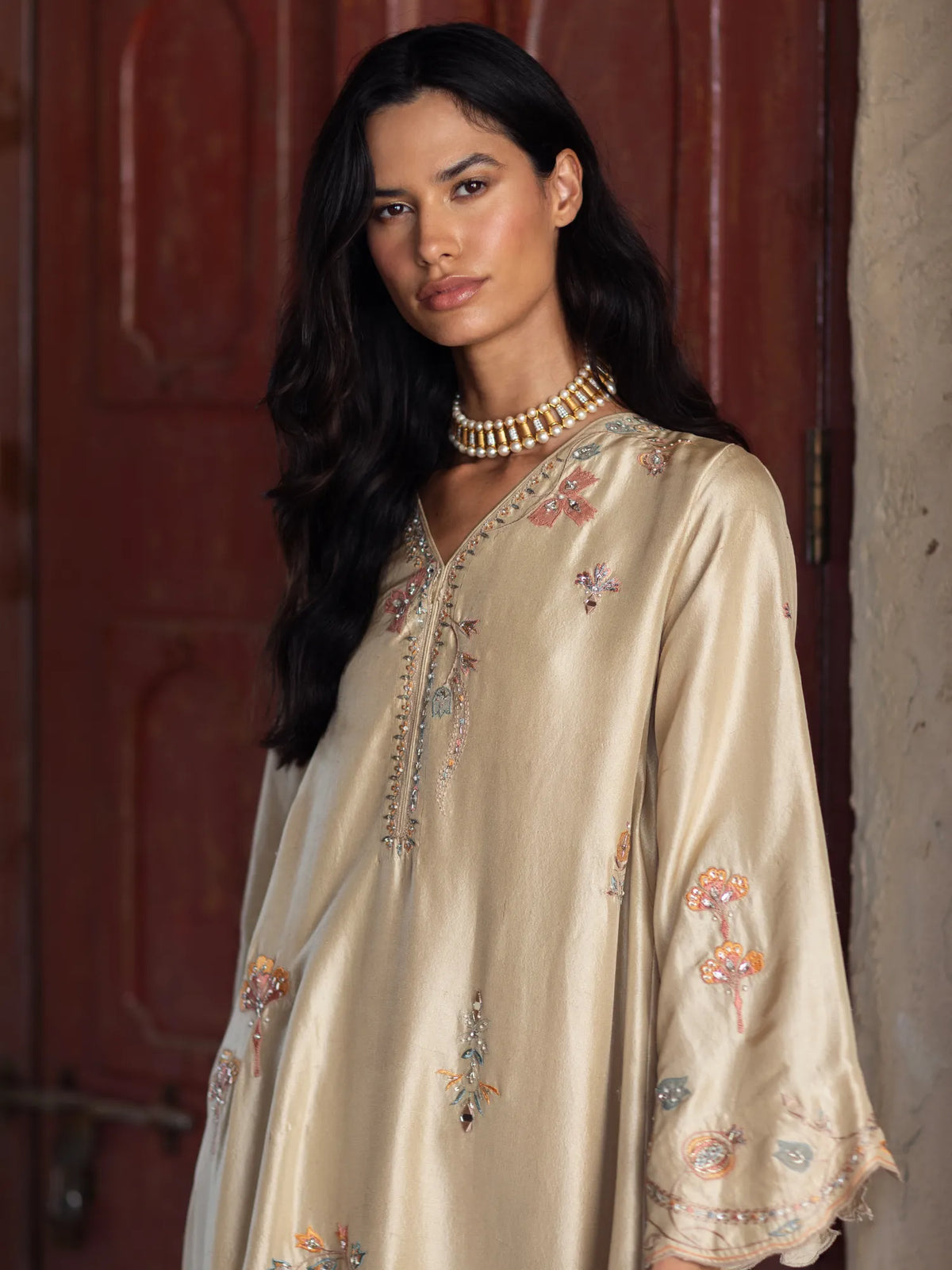 Woman wearing an embroidered beige dress with a textured wall background