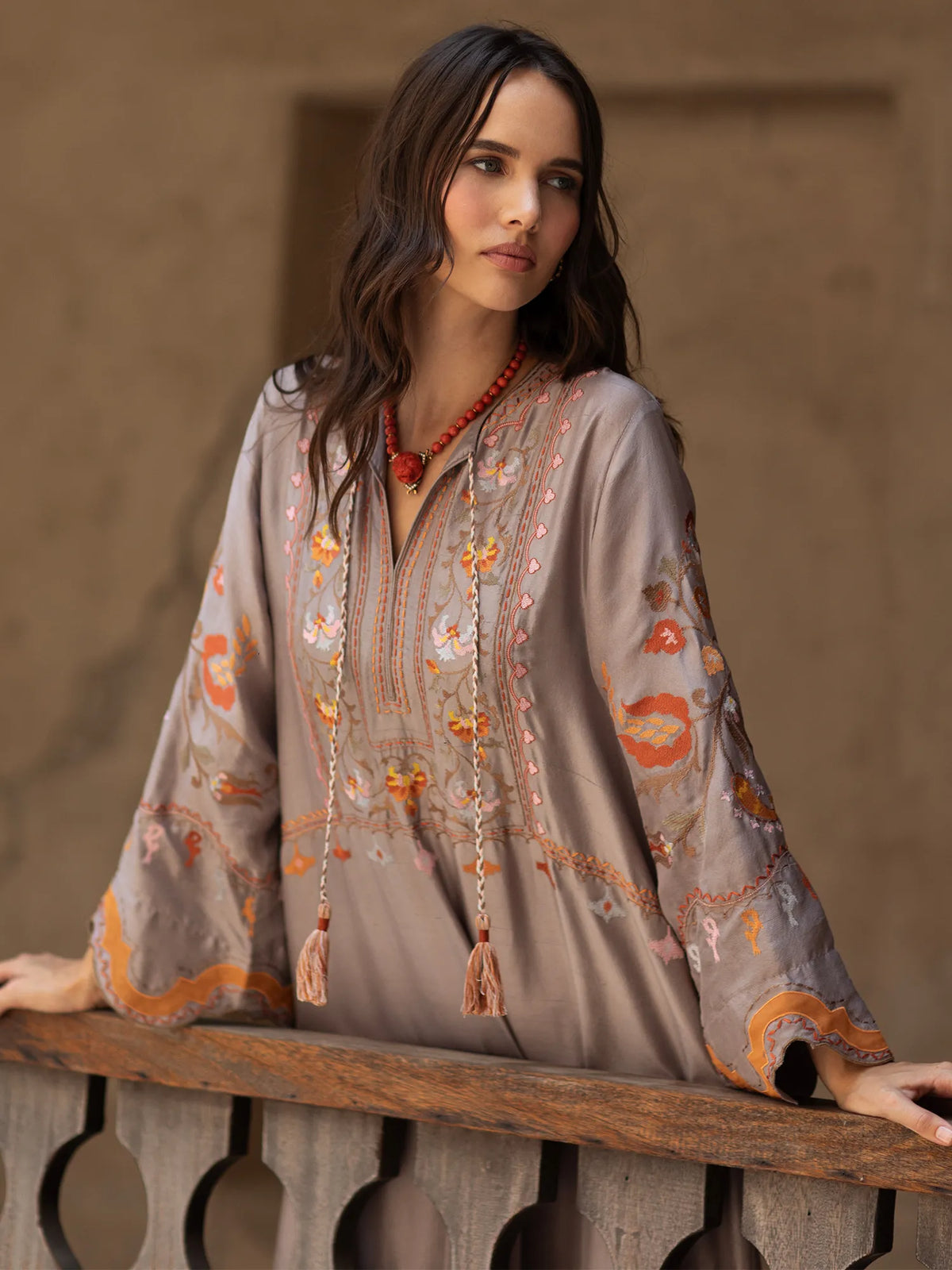 Woman wearing a beige embroidered blouse with orange details, standing against a neutral background.