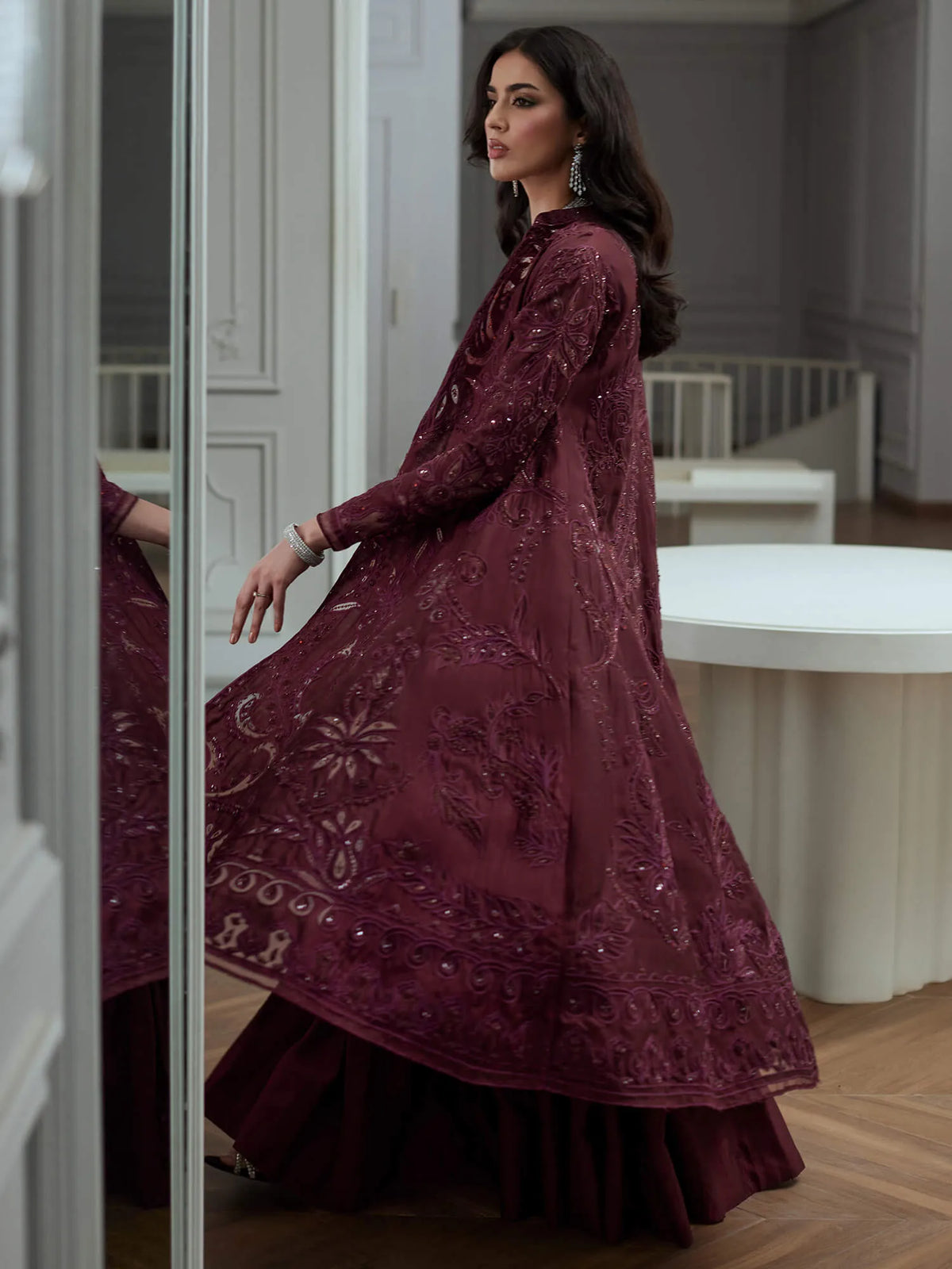 Woman wearing a burgundy embroidered dress in a room with white furniture.