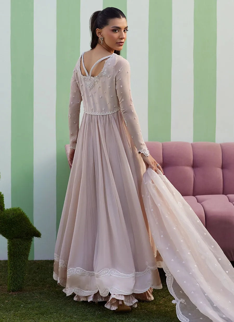 Woman in a long, light-colored dress standing in front of a striped wall with a pink couch.