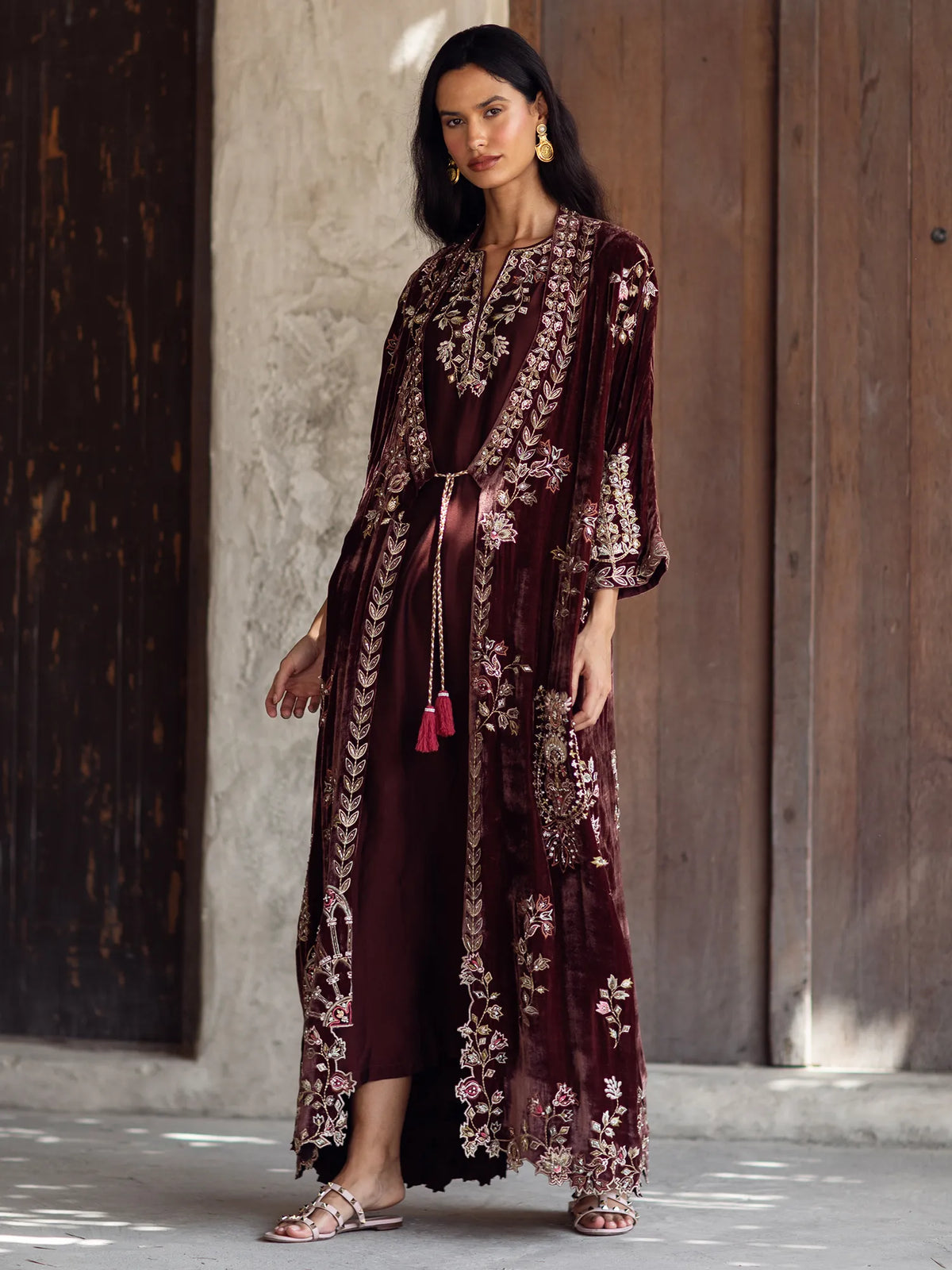 Woman wearing a burgundy embroidered dress with a wooden door in the background