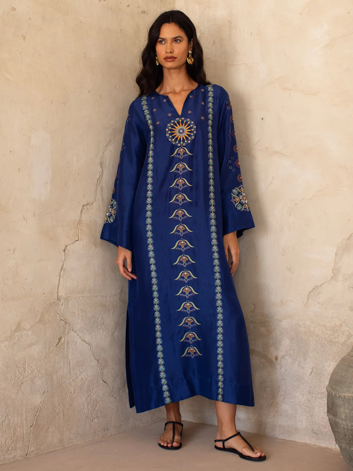 Woman wearing a blue embroidered dress against a beige wall