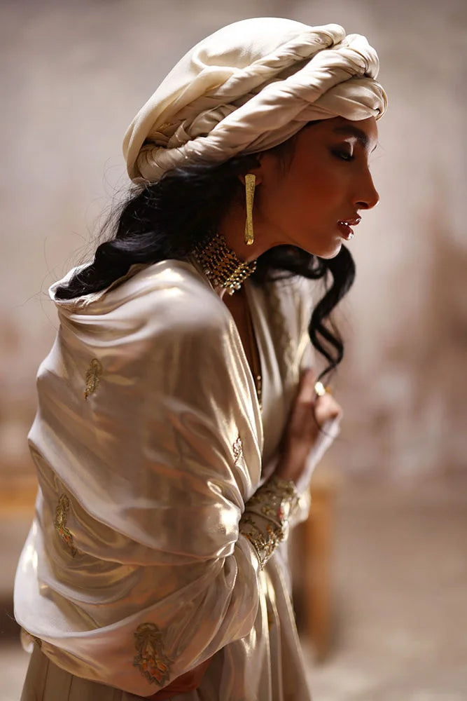 Woman in traditional attire with a turban and jewelry against a blurred background