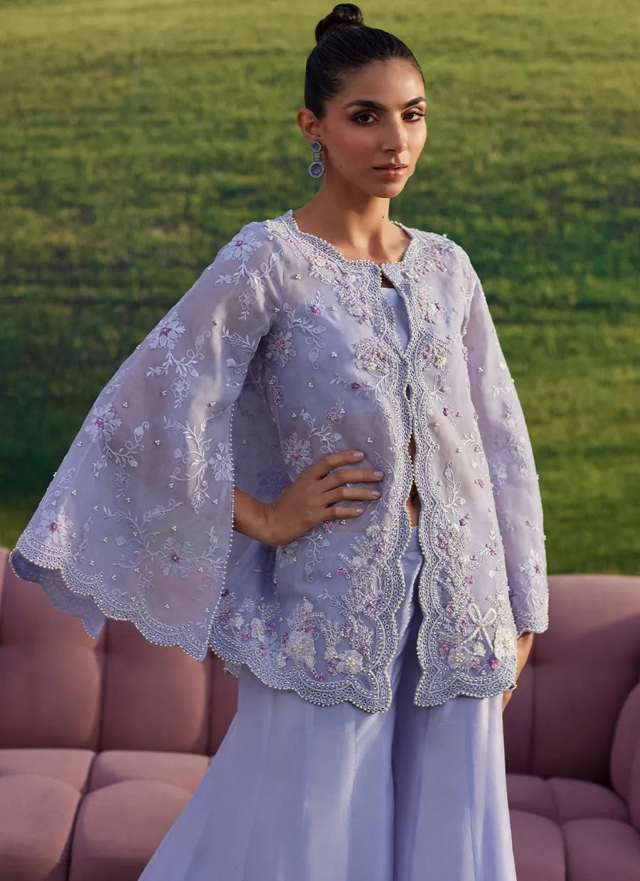 Woman in a light purple embroidered outfit standing outdoors with green grass in the background