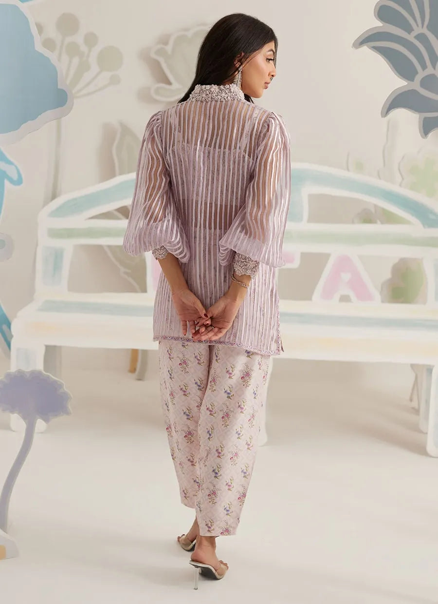 Woman wearing a striped shirt and floral pants standing in a room with decorative elements.