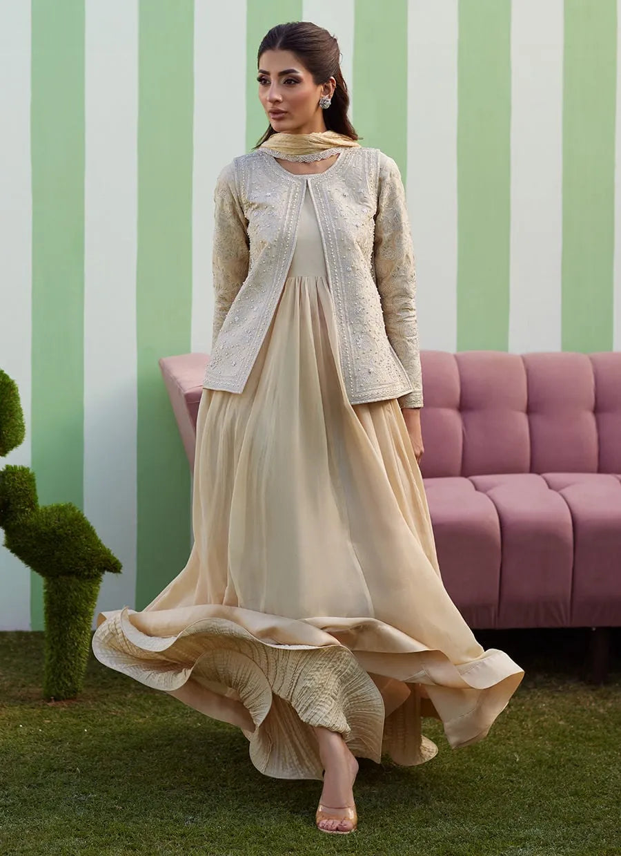 Woman in a beige outfit standing in front of a striped wall with a pink couch.