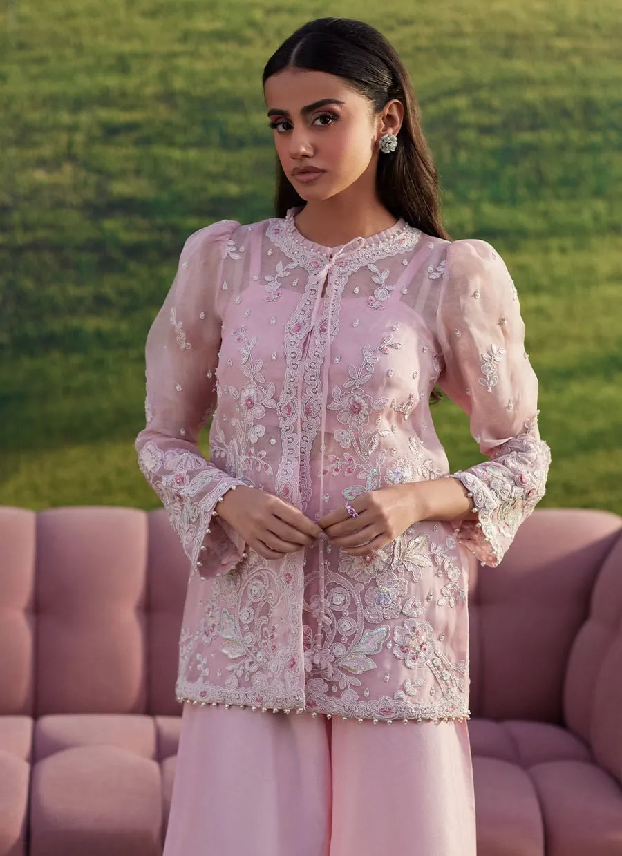 Woman wearing a pink embroidered outfit with a blurred green background