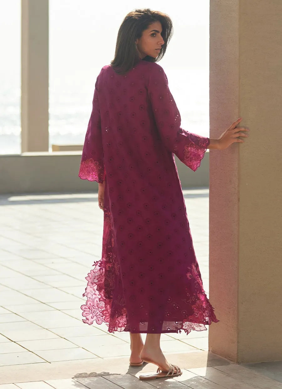 Woman in a long, burgundy lace dress standing by a window.