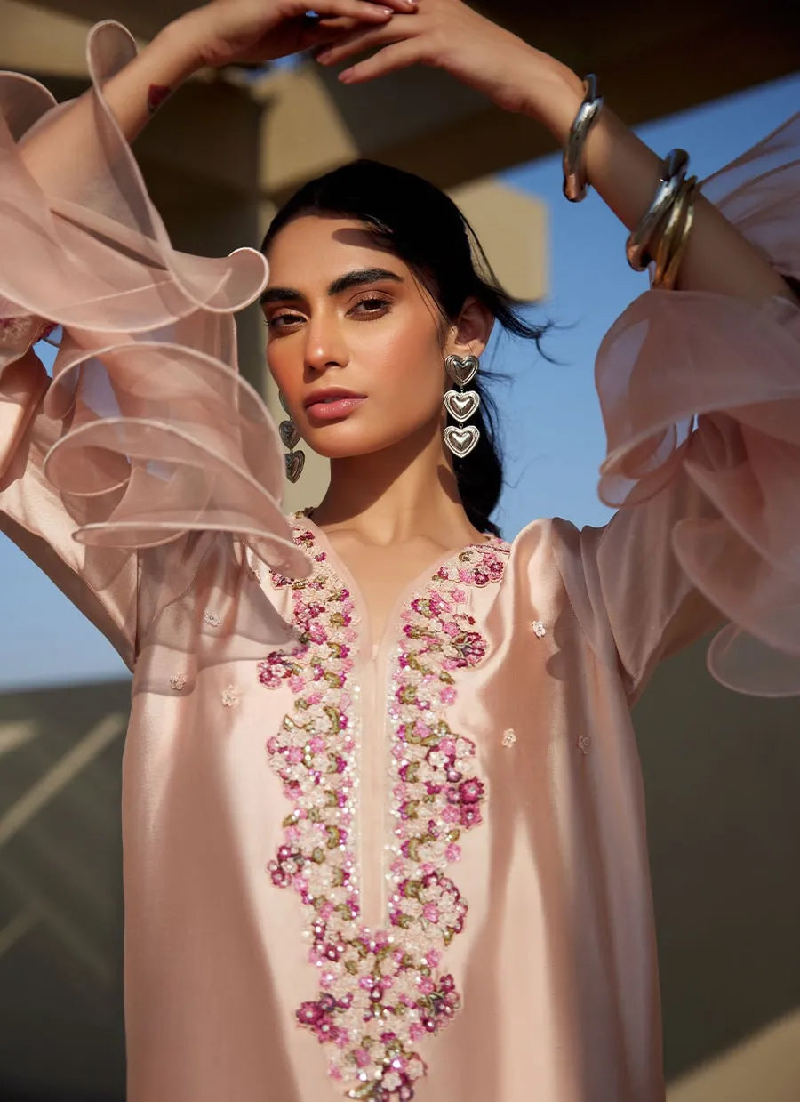 Woman wearing a light pink embroidered blouse with floral patterns, standing outdoors.