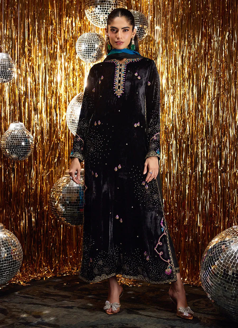 Woman in a black embroidered outfit holding disco balls against a gold curtain background