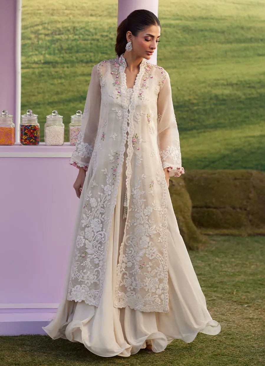 Woman in a cream embroidered outfit standing outdoors with a green field background