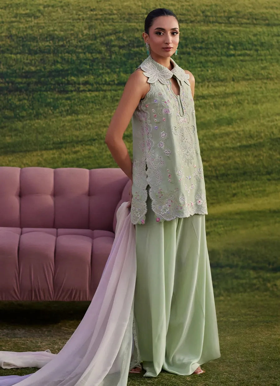 Woman in a light green outfit standing in a grassy field with a pink sofa in the background