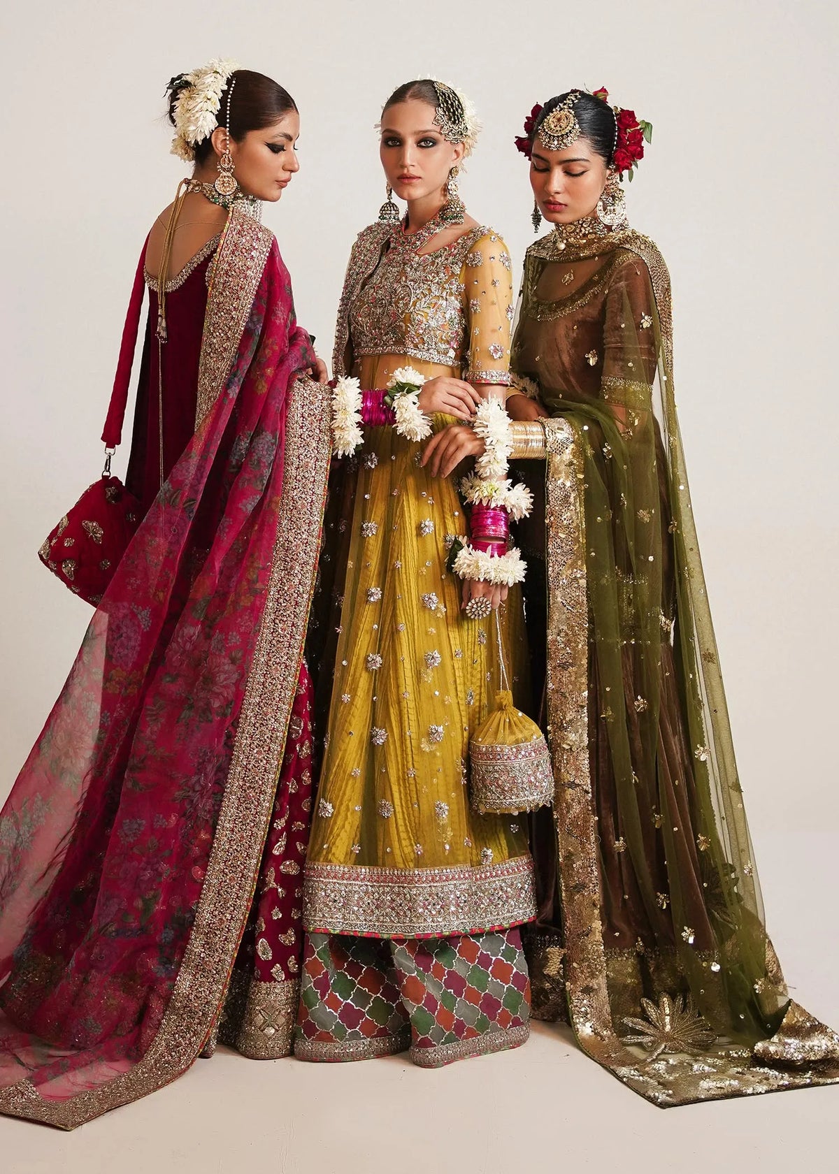 Three women in traditional Indian bridal attire with vibrant colors and intricate designs.