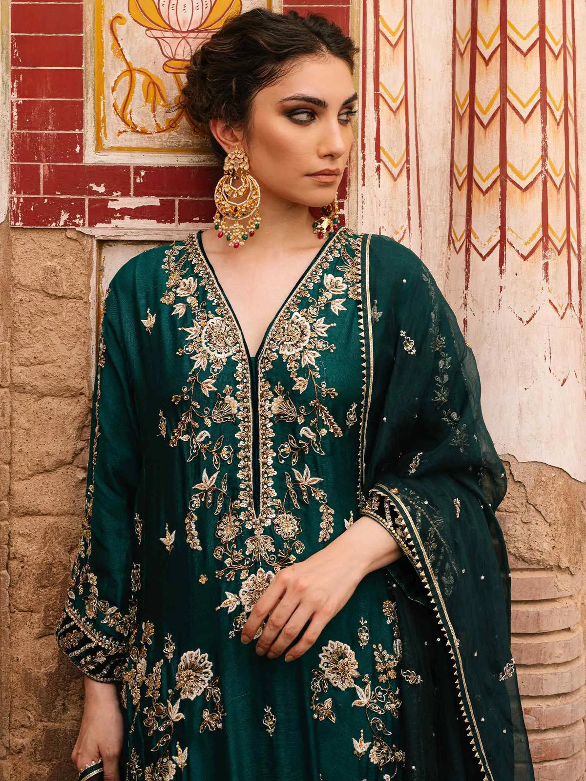 Woman in a green embroidered traditional outfit standing against a textured wall.