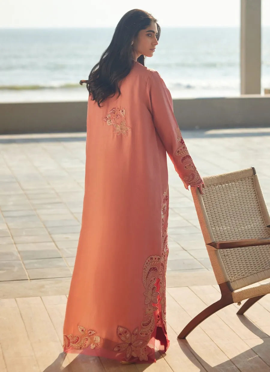 Woman in a peach-colored dress with floral embroidery standing by a poolside.