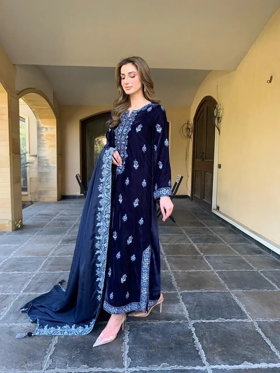 Woman in a navy blue embroidered outfit standing in an outdoor setting.