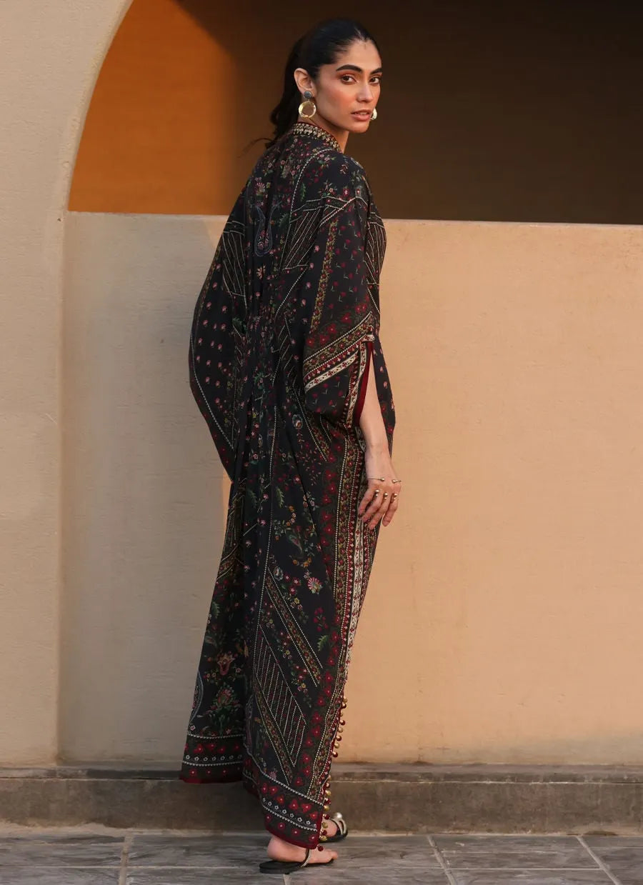 Woman in a traditional patterned outfit standing against a beige wall.