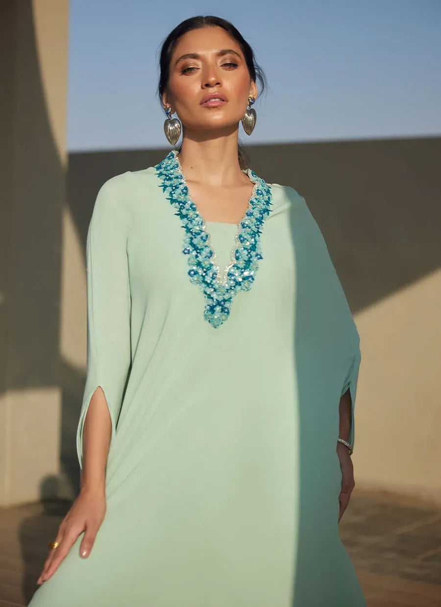 Woman wearing a light green dress with a blue necklace against a desert backdrop