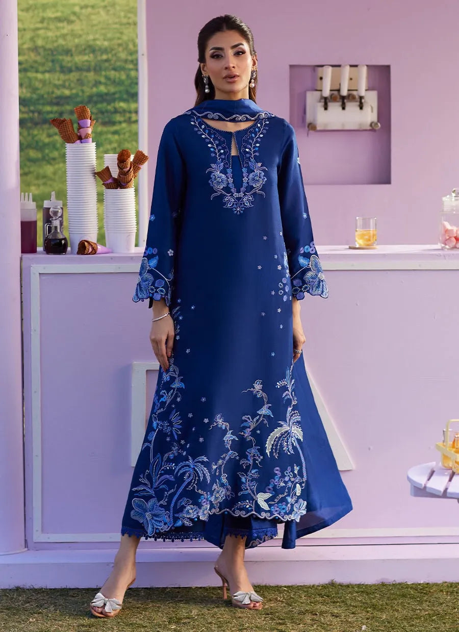 Woman wearing a blue embroidered dress standing in front of a purple wall with decorative items.