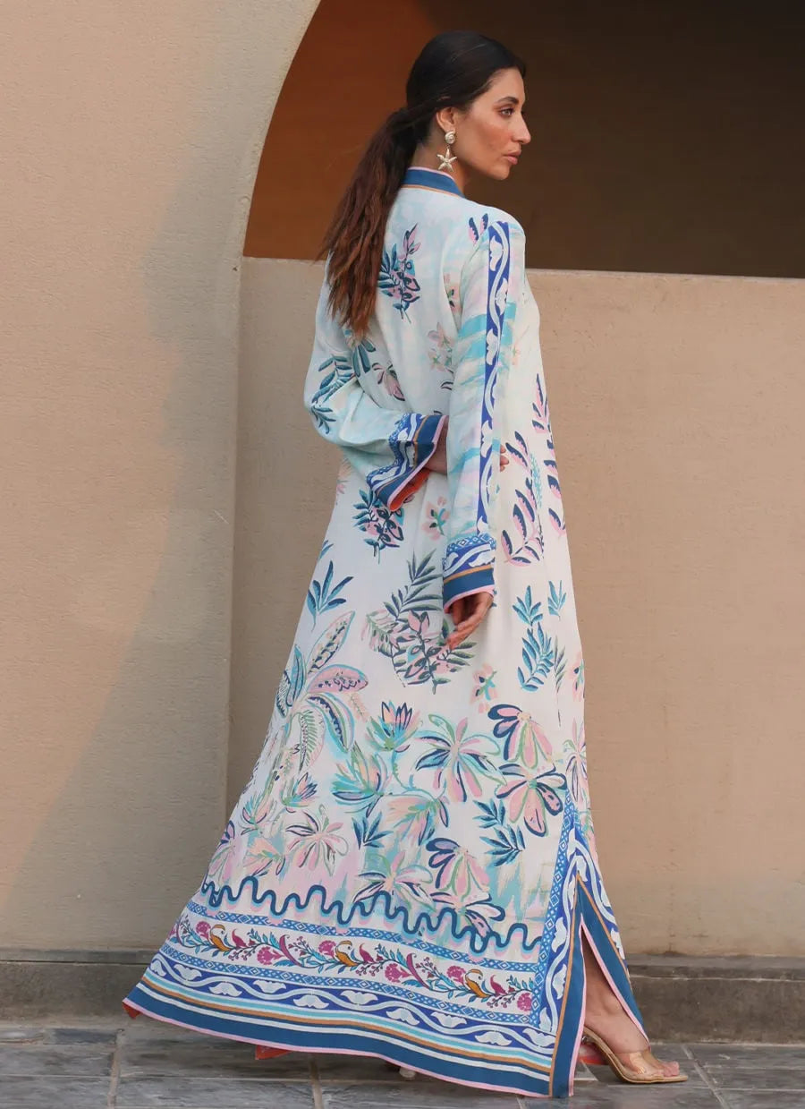Woman wearing a long, floral embroidered dress against a beige wall.