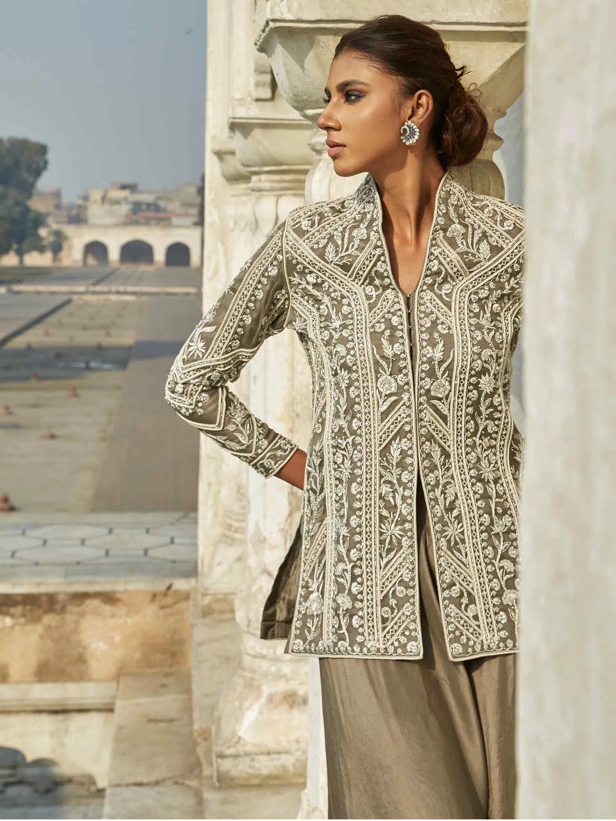 Woman wearing an embroidered jacket in front of a stone building.