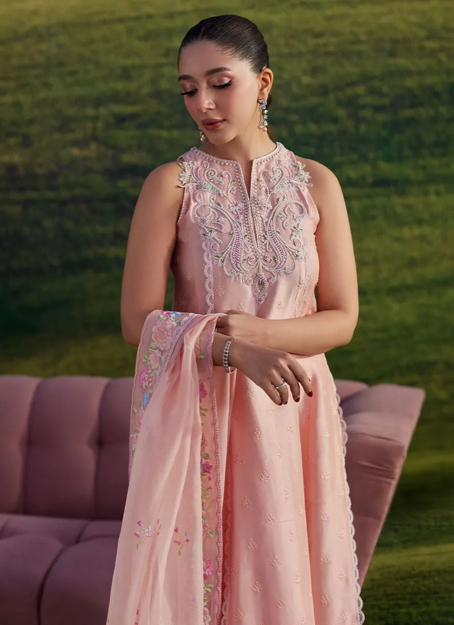 Woman in a pink embroidered dress holding a matching dupatta against a blurred green background