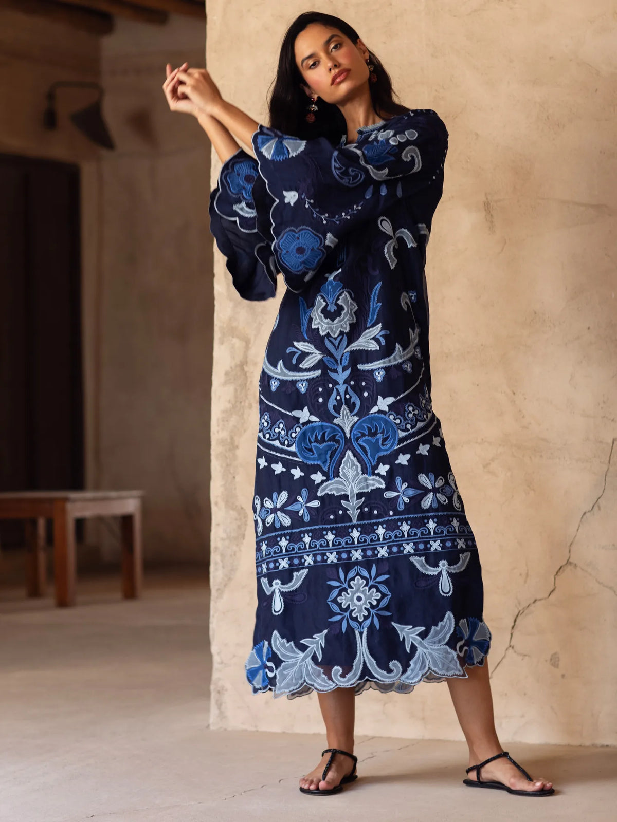 Woman wearing a blue patterned dress against a beige wall.
