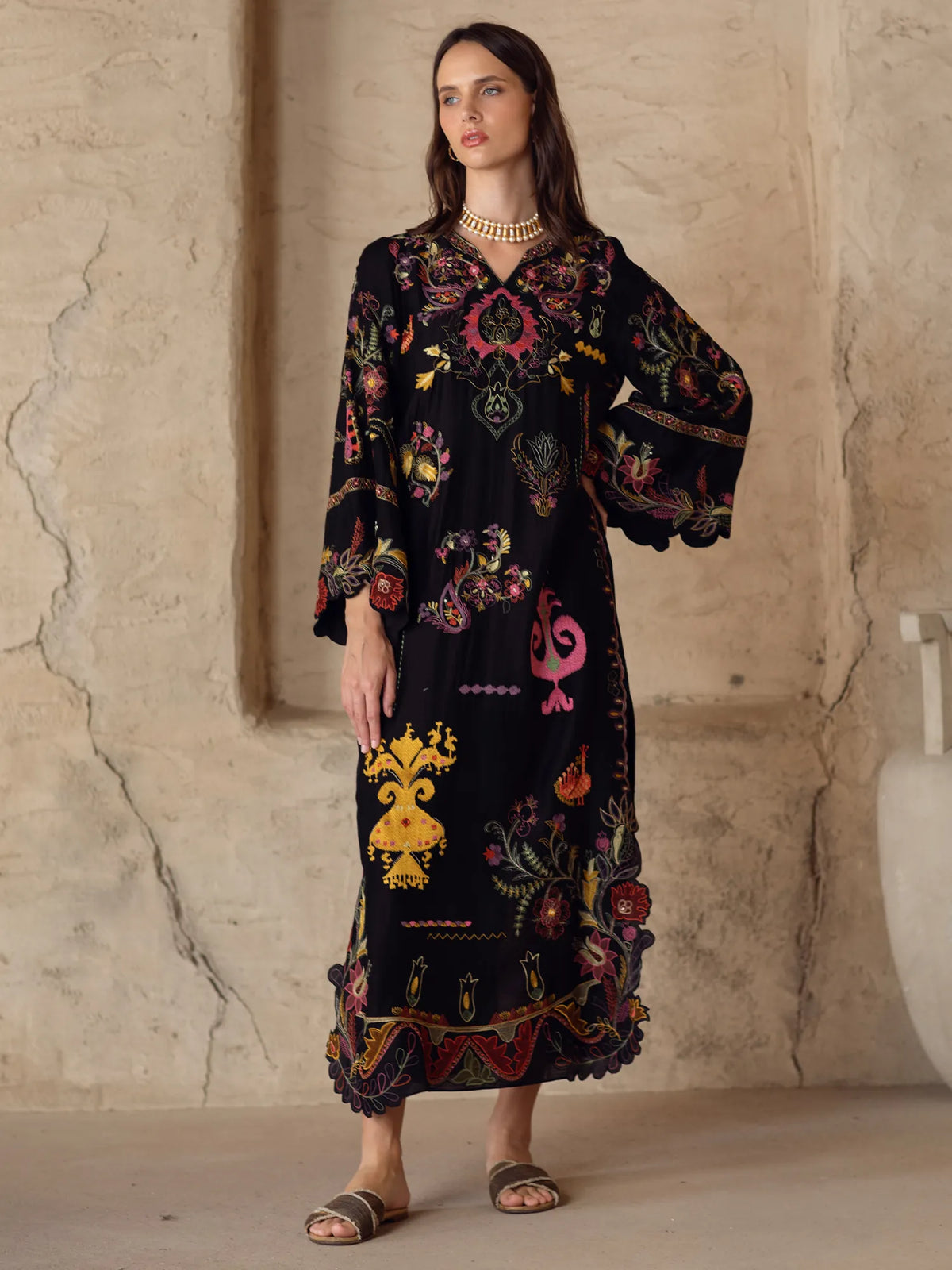 Woman wearing a black embroidered dress against a textured wall.