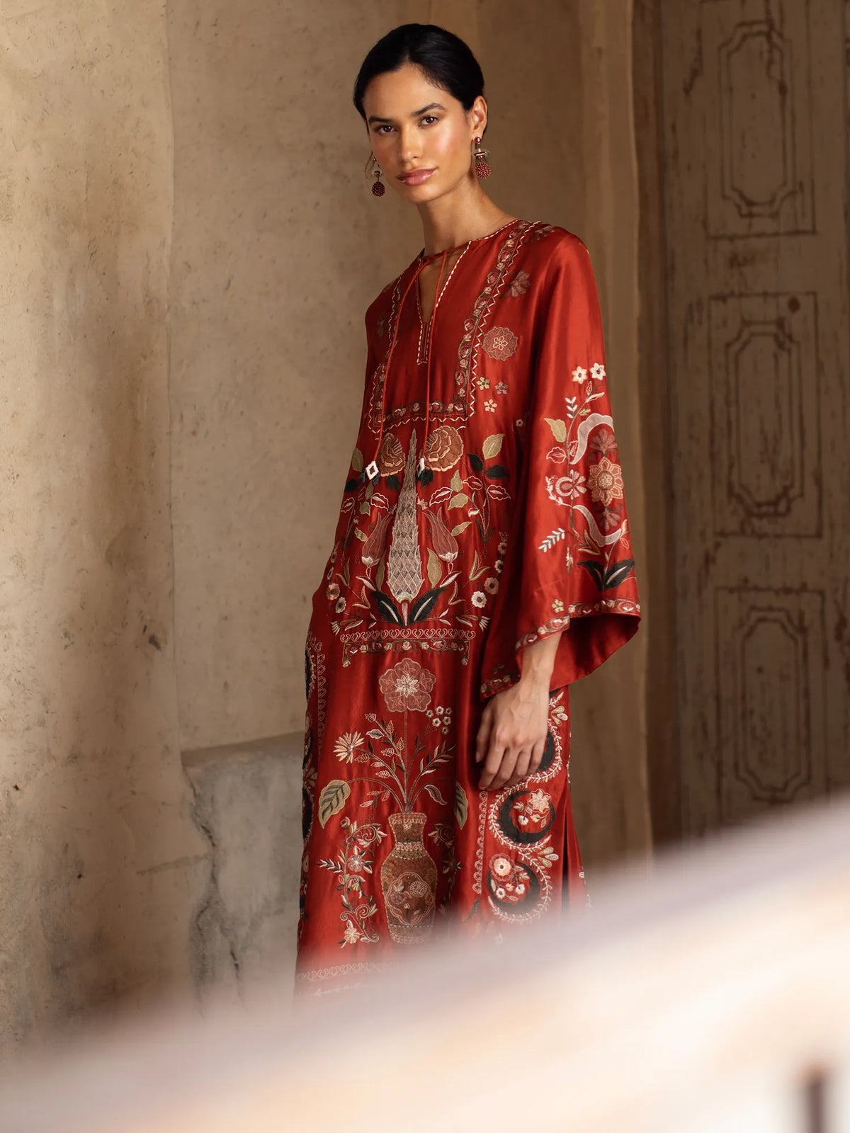 Woman wearing a red embroidered dress against a textured wall.
